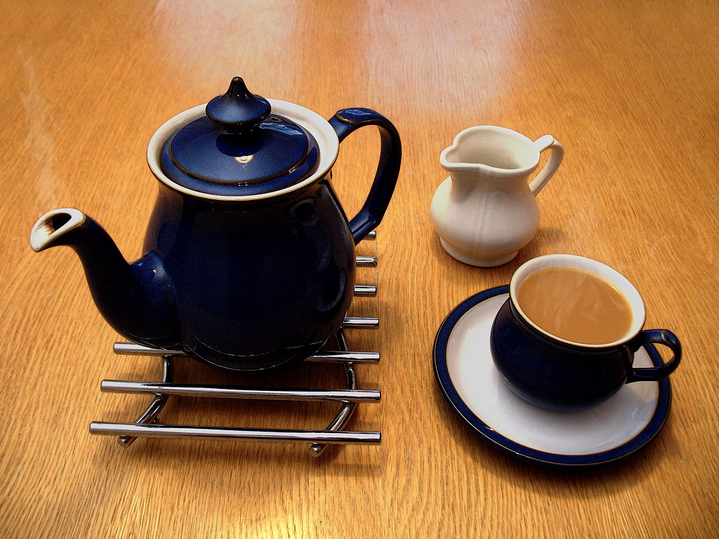 Una agradable taza de té con leche. Al lado, la tetera sobre un salvamanteles y una jarrita con leche.
